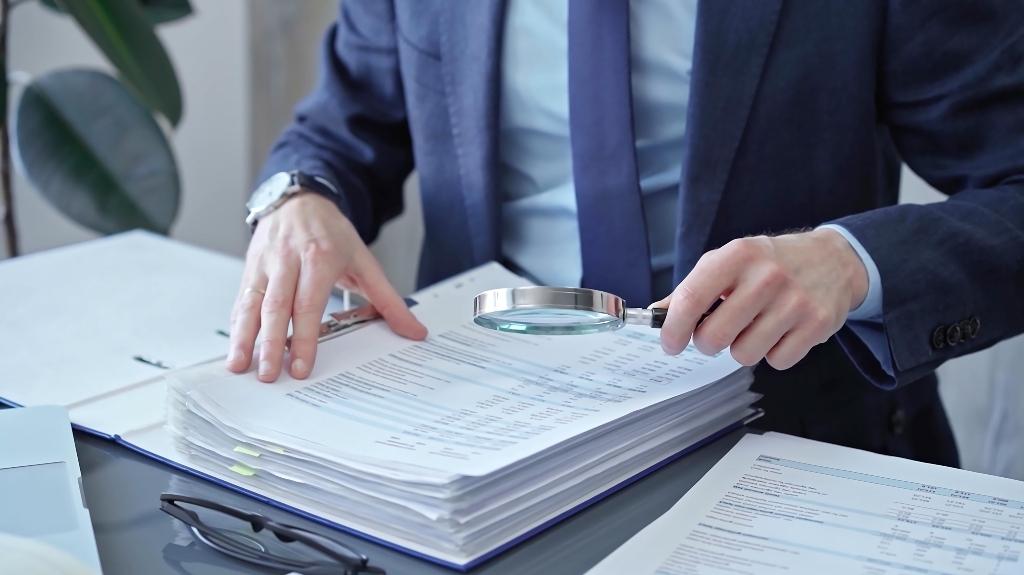 businessman examining documents with magnifying glass
