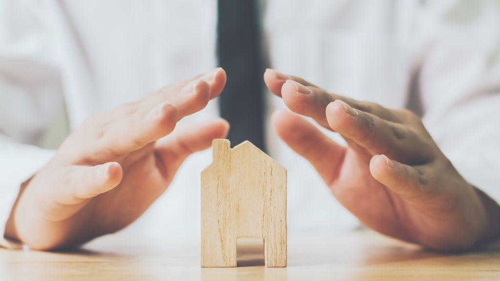 Man Protecting Small Model Home with Hands