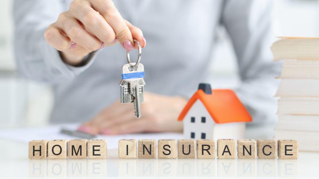 Person Holding Keys to a Home with Model Home and Blocks Spelling Home Insurance