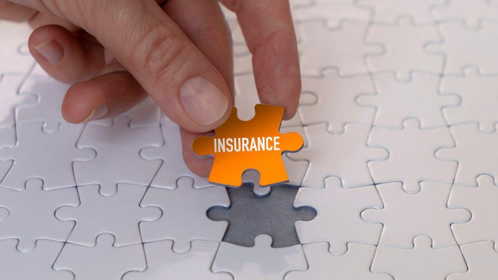 Hand Putting Orange Insurance Puzzle Piece in a White Puzzle