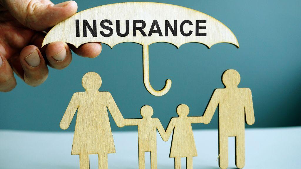Person Holding Insurance Umbrella Over Wooden Cutouts of a Family